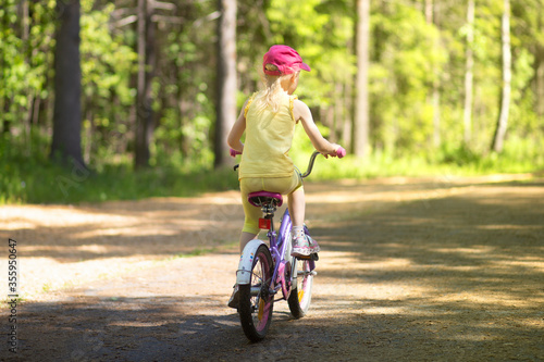 Fototapeta Naklejka Na Ścianę i Meble -  A girl rides a Bicycle on an asphalt road in the Park in the summer.