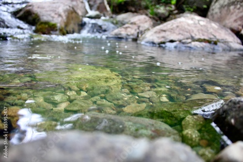Mountain river - a small waterfall on a river with crystal clear water that flows among gray stones in a green forest on a cloudy summer day. Big stones near the pond