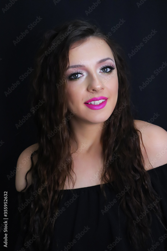 beautiful brunette young girl happily smiling, looking at camera with fresh make up on black background, pink lipstick curly hair over shoulders, in black dress studio shot, vertical image beautiful brunette young girl happily smiling, looking at camera with fresh make up on black background, pink lipstick curly hair over shoulders, in black dress studio shot, vertical image