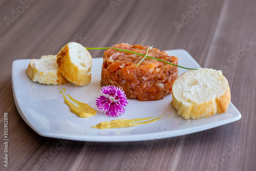 Homemade Salmon Tartare dish by amateur chef for culinary blogs, decorated with eatable purple flower and mostard. photo