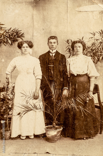 Fotografie Germany - CIRCA 1900s: Group portrait shot of two female and man in studio with palm tree plants