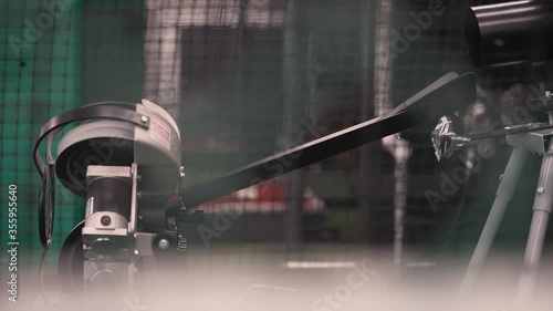 Baseball rolling down pitching machine ramp of indoor batting cage in slow motion