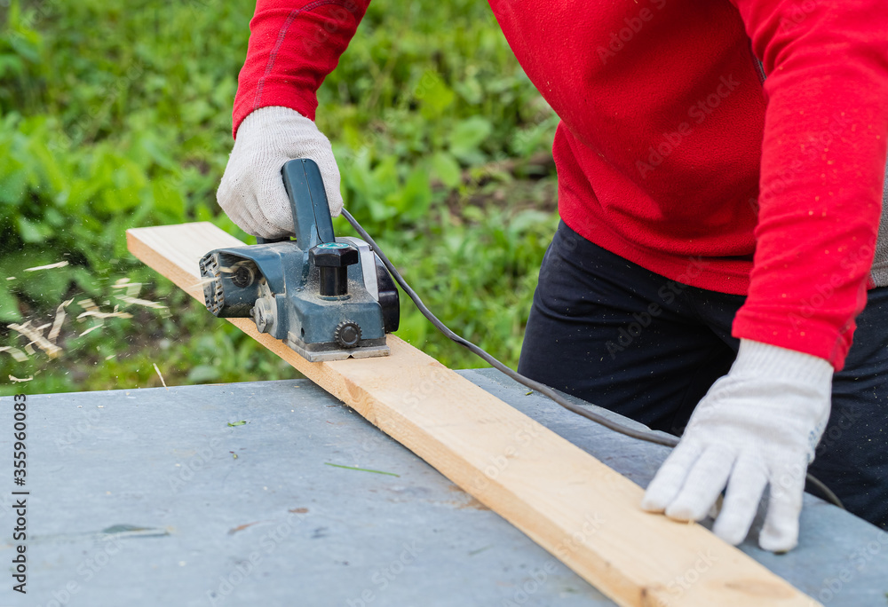 A man's hand holds an electric planing tool . The carpenter does the hardest work.