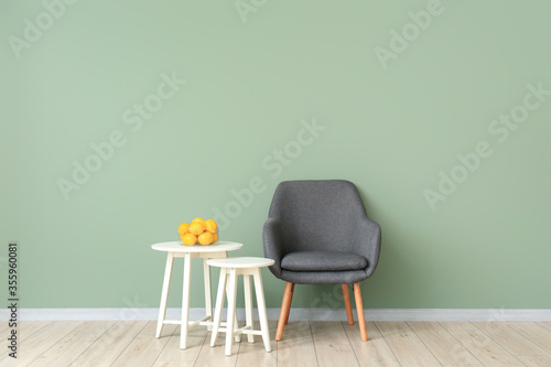 Fototapeta Naklejka Na Ścianę i Meble -  Stylish armchair with tables and lemon fruit near color wall in living room