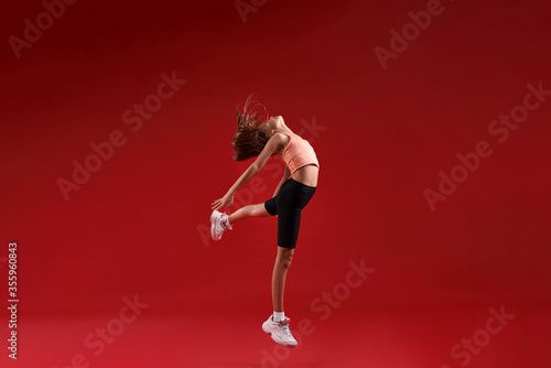 Practice with a purpose. A cute kid, girl is engaged in sport, she is looking up while jumping. Isolated on red background. Fitness, training, active lifestyle concept. Horizontal shot © Svitlana