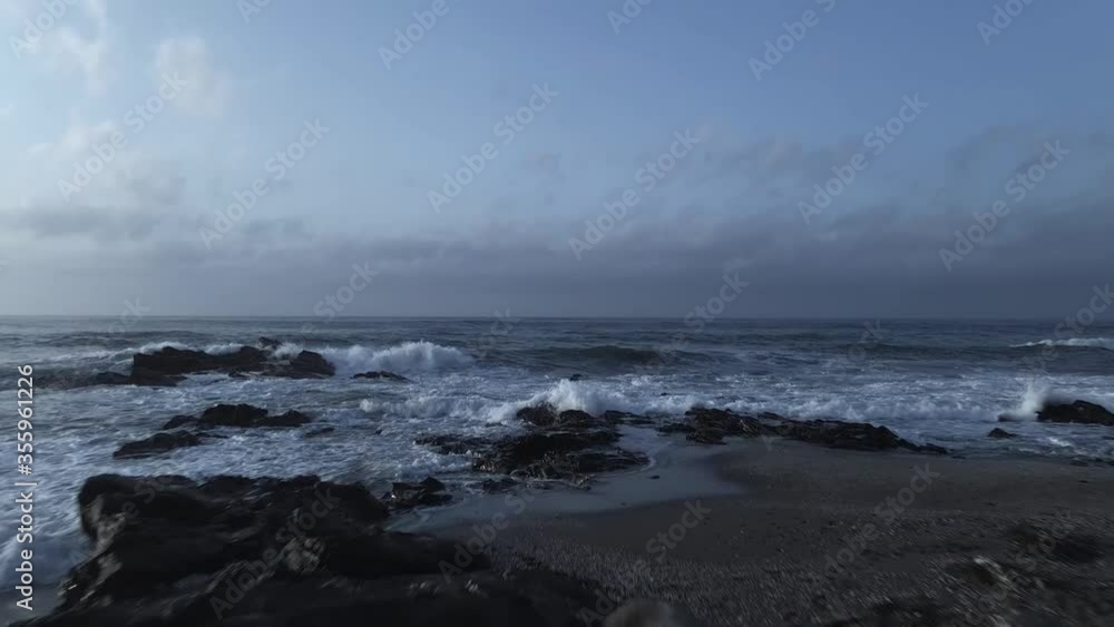 Aerial view with forward movement of blue ocean with waves washing up on dark empty beach, in Playa Penon Del Cura Spain Aerial view with forward movement of blue ocean with waves washing up on dark empty beach, in Playa Penon Del Cura Spain