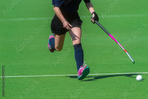 Field hockey player, in possesion of the ball, running over an astroturf pitch, looking for a team mate to pass to
