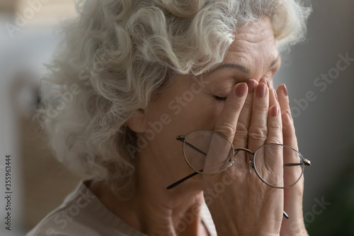 Close up of tired elderly woman rub massage eyes take off glasses suffering from headache or migraine, exhausted mature 60s female have dizziness or blurry vision form high blood pressure photo