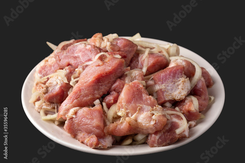 Uncooked pork meat with onion, salt and pepper on a plate isolated on dark background