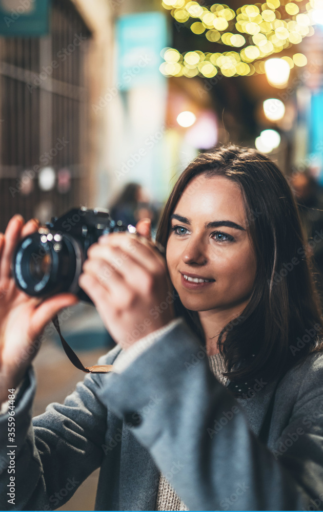 Photographer young girl with retro camera take photo on background bokeh light in night city,  photo hobby