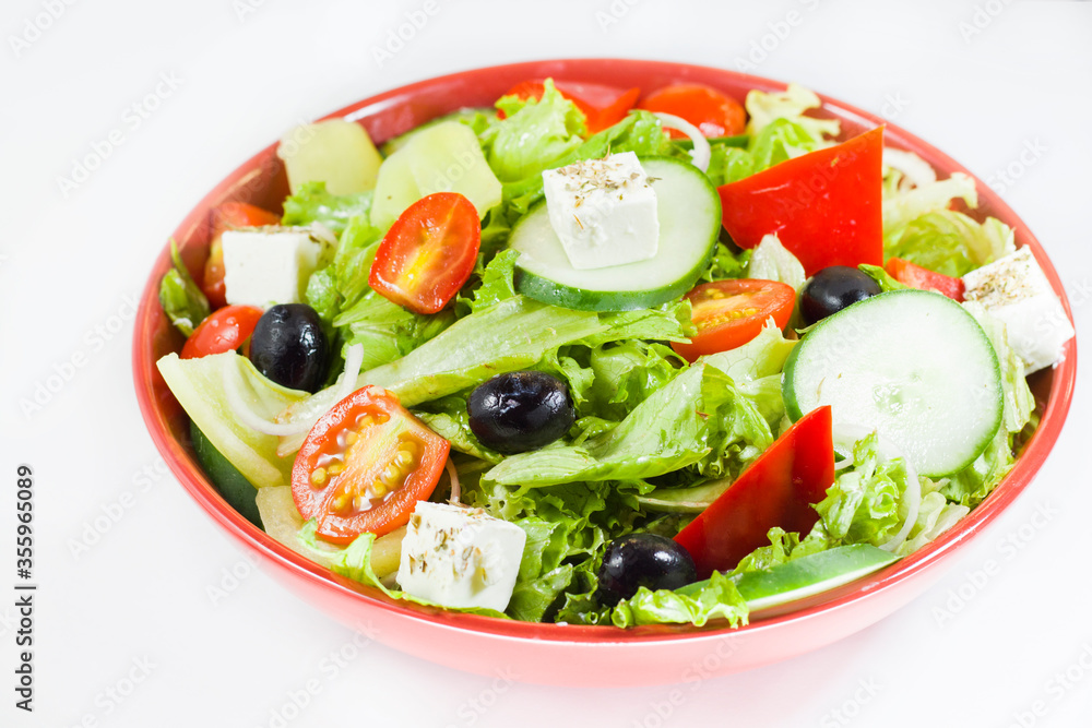 Vegetable salad on the plate, tomatoes, green salad, cheese, lemon and olive, other vegetables.