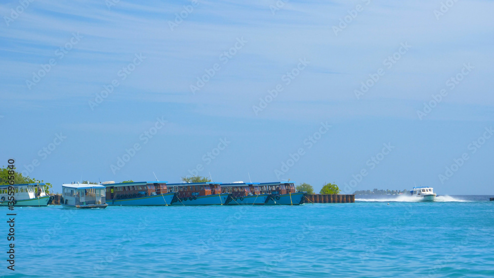 Water taxi speeds past other boats anchored along an exotic island coastline.