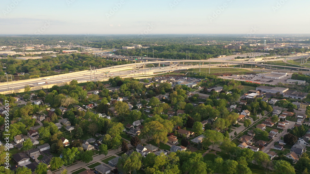 Aerial view of american suburb, highway at summertime.  Establishing shot of american neighborhood. Real estate, residential houses, freeway, traffic. Drone shot, from above