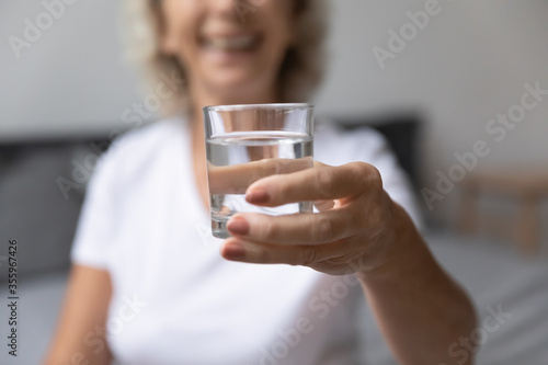 Close up mature woman hold recommend drinking daily dose of clear pure still water for body balance or refreshment, happy senior female enjoy clean mineral aqua, elderly healthy lifestyle concept