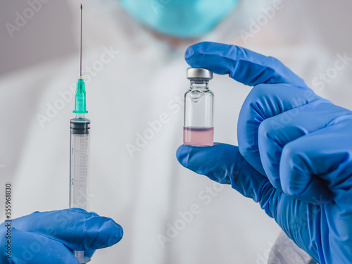 A doctor holds the Covid-19 vaccine and an injection with blue medical gloves.