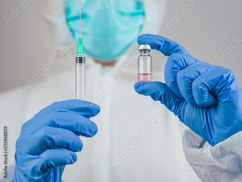 A doctor holds the Covid-19 vaccine and an injection with blue medical gloves.