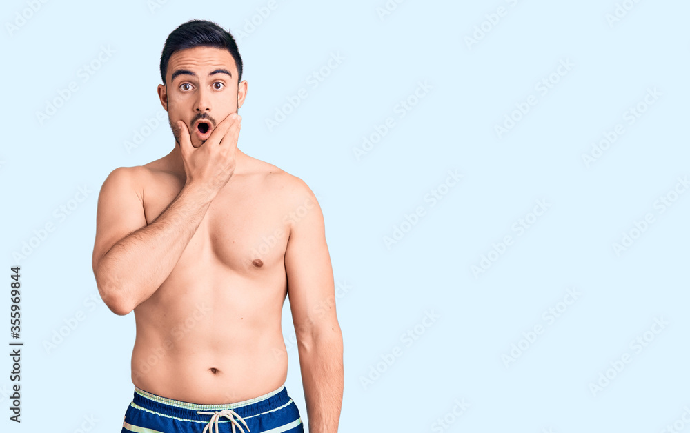Fototapeta premium Young handsome man wearing swimwear looking fascinated with disbelief, surprise and amazed expression with hands on chin