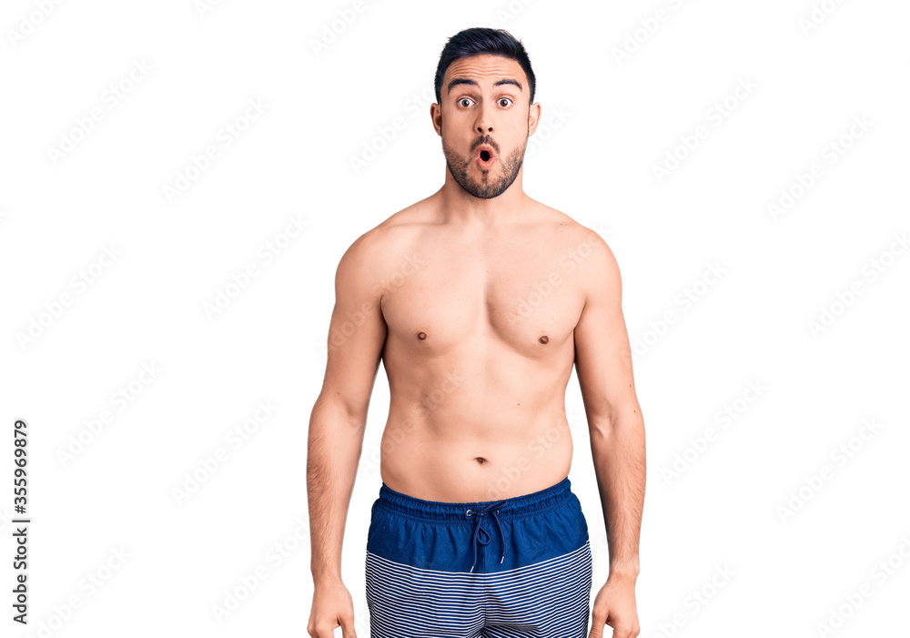 Young handsome man wearing swimwear scared and amazed with open mouth for surprise, disbelief face Young handsome man wearing swimwear scared and amazed with open mouth for surprise, disbelief face