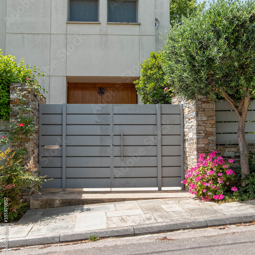 elegant house entrance metallic grey door by the sidewalk with plenty of foliage and colorful flowers