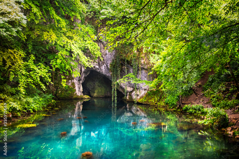 Naklejka premium Pond on wellhead of river surrounded with forest and cave on Krupajsko vrelo in Serbia. Beautiful turquoise water.