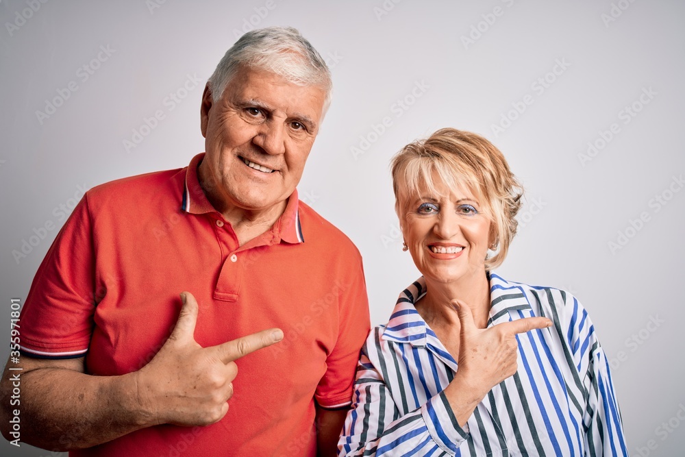 Senior beautiful couple standing together over isolated white background cheerful with a smile on face pointing with hand and finger up to the side with happy and natural expression Senior beautiful couple standing together over isolated white background cheerful with a smile on face pointing with hand and finger up to the side with happy and natural expression