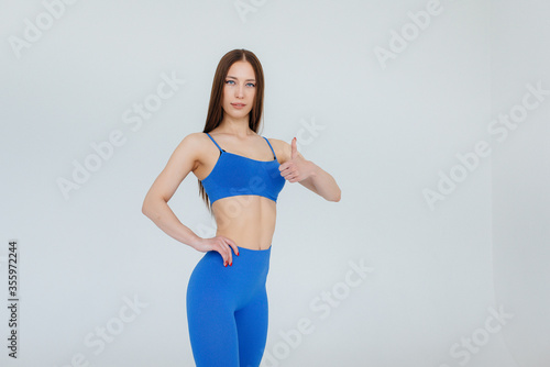 Sexy young girl posing in a blue tracksuit on a white background. Fitness, healthy lifestyle