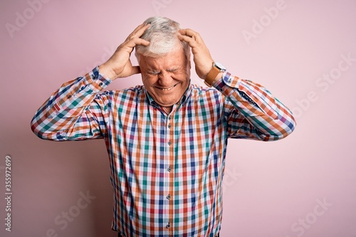 Senior handsome hoary man wearing casual colorful shirt over isolated pink background suffering from headache desperate and stressed because pain and migraine. Hands on head.