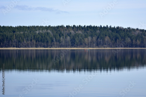 Leningradskaya oblast Russia, May 05 2016. The mirror surface of the lake's water reflectsgreen forest standing on the opposite shore. A place to relax in countryside