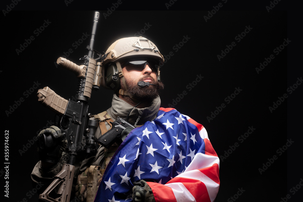 Fototapeta premium American special forces against a dark background, a soldier in military equipment holds weapons and the flag of the United States of America, elite troops