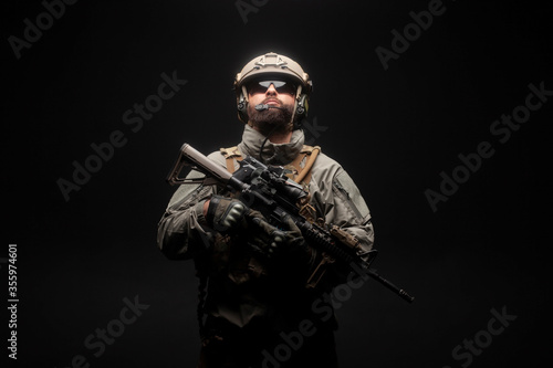 American modern special forces against a dark background, a soldier in military equipment holds weapons and looks up, elite troops