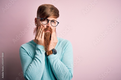 Fototapeta Naklejka Na Ścianę i Meble -  Handsome Irish redhead man with beard wearing glasses over pink isolated background Tired hands covering face, depression and sadness, upset and irritated for problem