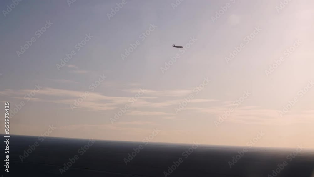View out of an airplanes left side window seing another aircraft nearby flying the same direction in sunset.