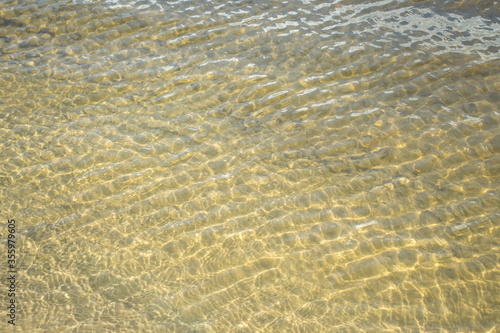 Abstract background of the ripples on water at the beach. Transparent sea water. Soft wave of ocean on sandy beach. Yellow background. 