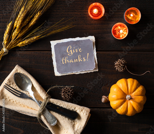 Thanksgiving Table Place Setting with Vintage Silverware, Lighted Candles, wheat and pumpkin, all on Dark Rustic Wood Table.  The card text says Give Thanks photo