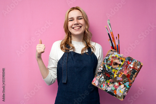 cheerful girl artist shows her hand like and smiles on a pink background, great profession artist photo