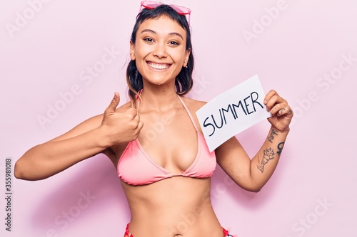 Young woman wearing summer hat smiling happy and positive, thumb up doing excellent and approval sign