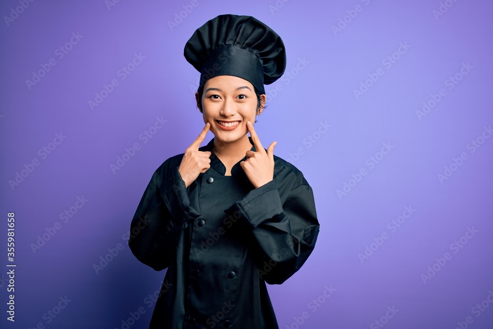 Young beautiful chinese chef woman wearing cooker uniform and hat over purple background Smiling with open mouth, fingers pointing and forcing cheerful smile Young beautiful chinese chef woman wearing cooker uniform and hat over purple background Smiling with open mouth, fingers pointing and forcing cheerful smile