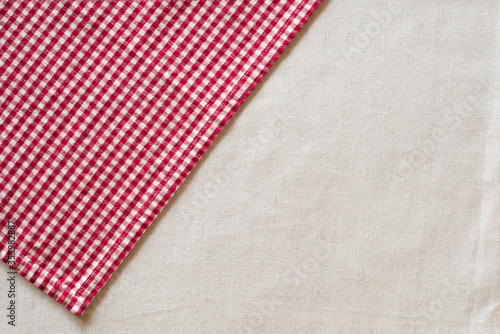 Red and White Checked Cloth at angle on upper corner of off white or cream colored linen table cloth. Horizontal above view with room or space for copy, text or your words or design