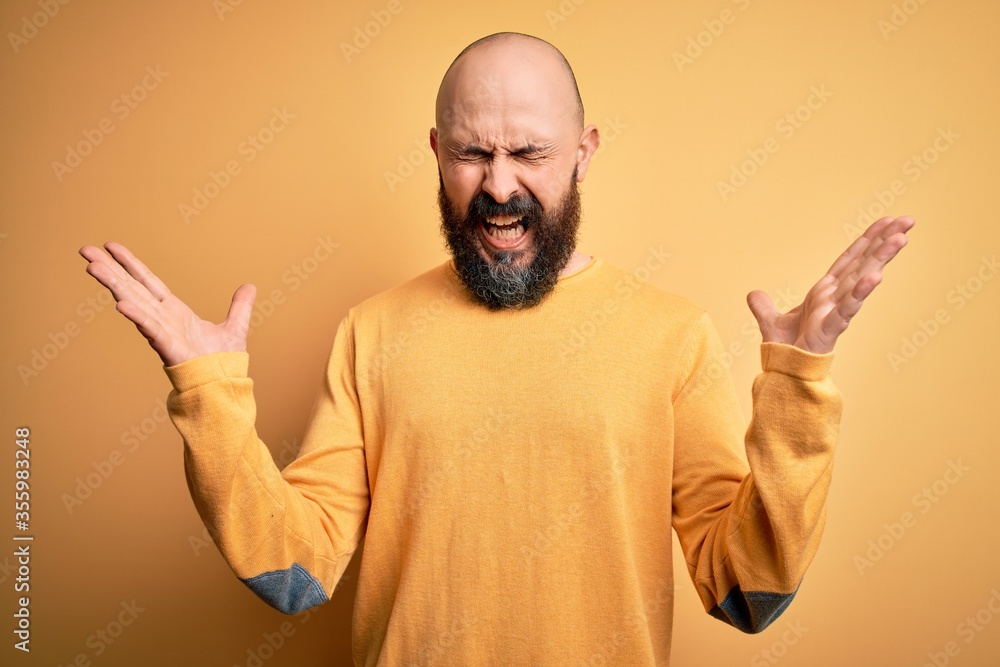 Handsome bald man with beard wearing casual sweater standing over yellow background celebrating mad and crazy for success with arms raised and closed eyes screaming excited. Winner concept Handsome bald man with beard wearing casual sweater standing over yellow background celebrating mad and crazy for success with arms raised and closed eyes screaming excited. Winner concept