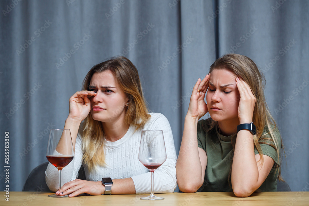 Two best friends. Young European-looking women having a conversation sitting at a desk holding a glass of wine. beautiful girls sisters love to drink alcohol laughing cheerful relax in the living room Two best friends. Young European-looking women having a conversation sitting at a desk holding a glass of wine. beautiful girls sisters love to drink alcohol laughing cheerful relax in the living room