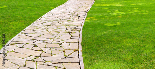 Canvas Print flagstone footpath in a park with a green lawn goes into perspective on a sunny summer day, closeup of brown paving stone tiles with copy space 16:9