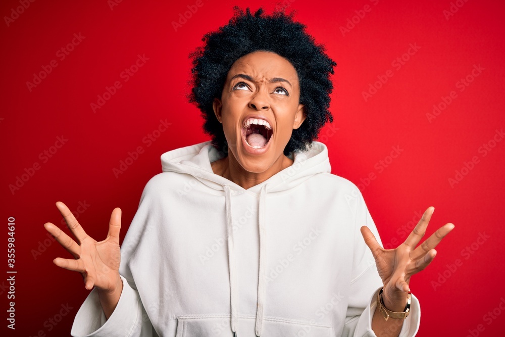 Young beautiful African American afro sportswoman with curly hair wearing sportswear crazy and mad shouting and yelling with aggressive expression and arms raised. Frustration concept. Young beautiful African American afro sportswoman with curly hair wearing sportswear crazy and mad shouting and yelling with aggressive expression and arms raised. Frustration concept.