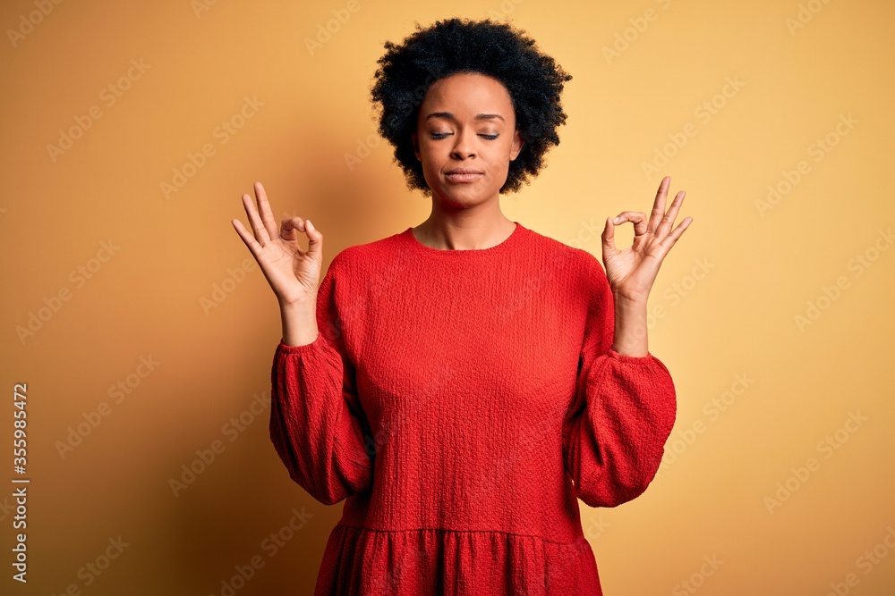 Young beautiful African American afro woman with curly hair wearing casual sweater relax and smiling with eyes closed doing meditation gesture with fingers. Yoga concept. Young beautiful African American afro woman with curly hair wearing casual sweater relax and smiling with eyes closed doing meditation gesture with fingers. Yoga concept.