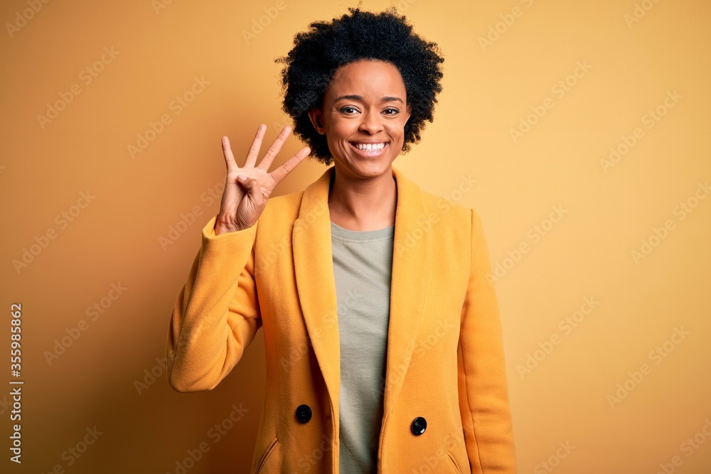 Young beautiful African American afro businesswoman with curly hair wearing yellow jacket showing and pointing up with fingers number four while smiling confident and happy. Young beautiful African American afro businesswoman with curly hair wearing yellow jacket showing and pointing up with fingers number four while smiling confident and happy.