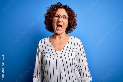 Middle age beautiful curly hair woman wearing casual striped shirt over isolated background winking looking at the camera with sexy expression, cheerful and happy face.