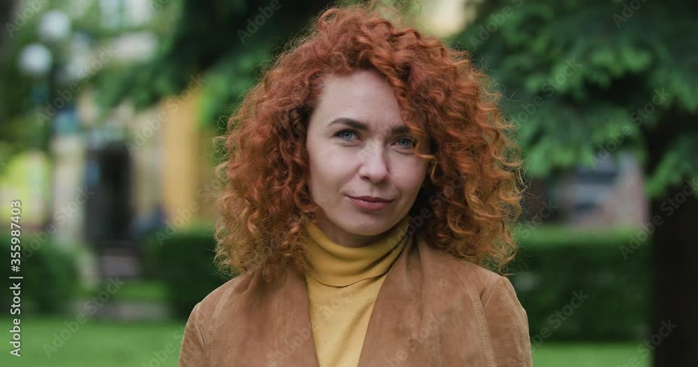 Attractive red-haired woman with curly hair looks at the camera and says something, close up slow motion Attractive red-haired woman with curly hair looks at the camera and says something, close up slow motion