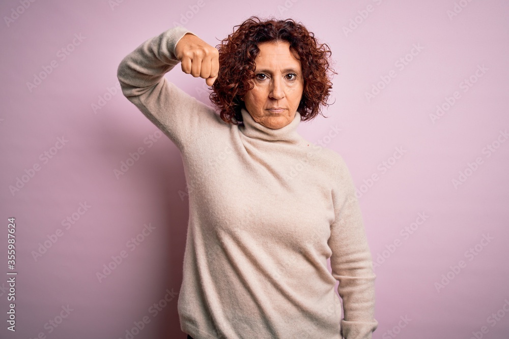 Middle age beautiful curly hair woman wearing casual turtleneck sweater over pink background Strong person showing arm muscle, confident and proud of power Middle age beautiful curly hair woman wearing casual turtleneck sweater over pink background Strong person showing arm muscle, confident and proud of power