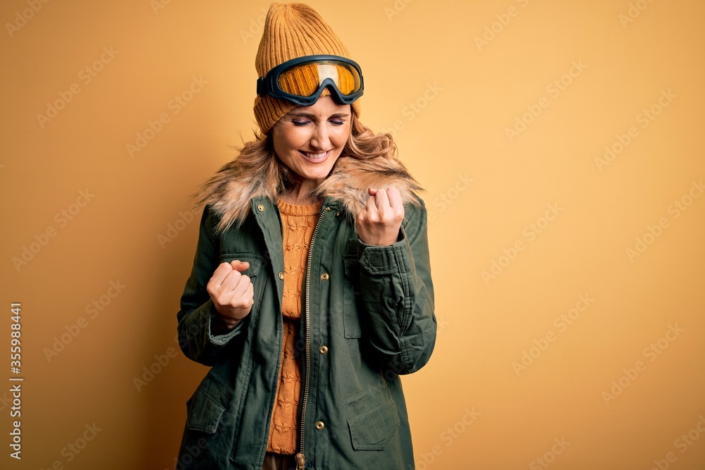 Middle age beautiful blonde skier woman wearing snow sportwear and ski goggles celebrating surprised and amazed for success with arms raised and eyes closed. Winner concept. Middle age beautiful blonde skier woman wearing snow sportwear and ski goggles celebrating surprised and amazed for success with arms raised and eyes closed. Winner concept.