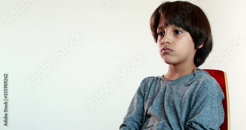 Pensive child boy sitting on chair thinking, kid crossing arms feeling upset emotion