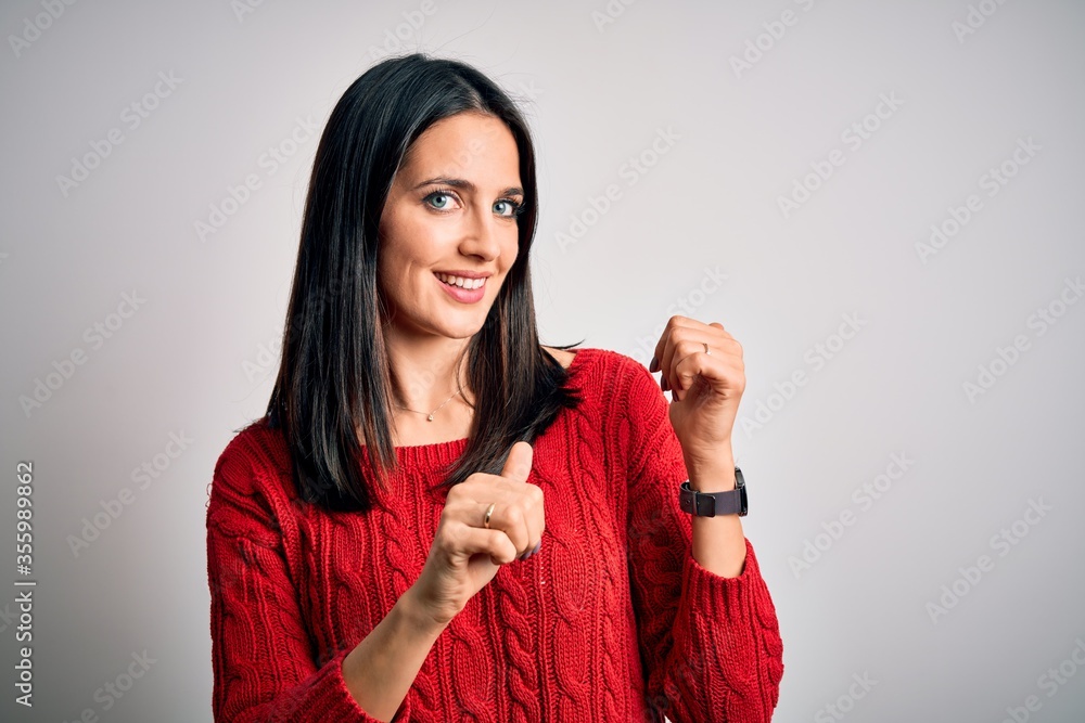 Young brunette woman with blue eyes wearing casual sweater over isolated white background Pointing to the back behind with hand and thumbs up, smiling confident Young brunette woman with blue eyes wearing casual sweater over isolated white background Pointing to the back behind with hand and thumbs up, smiling confident